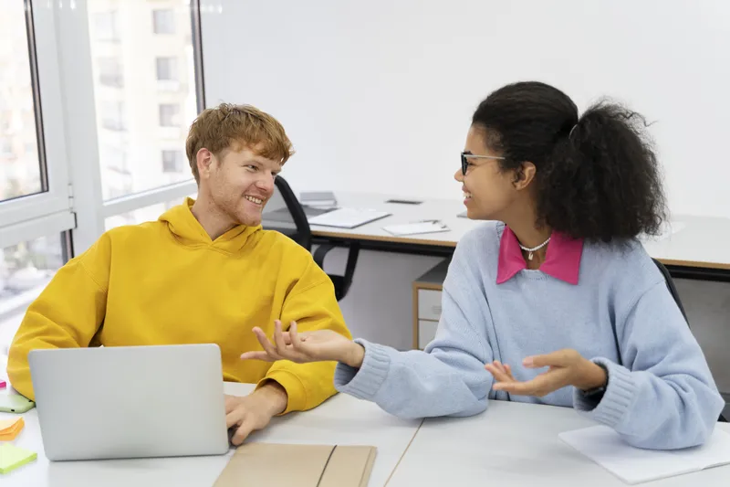 Two colleagues discuss their work together at a shared desk